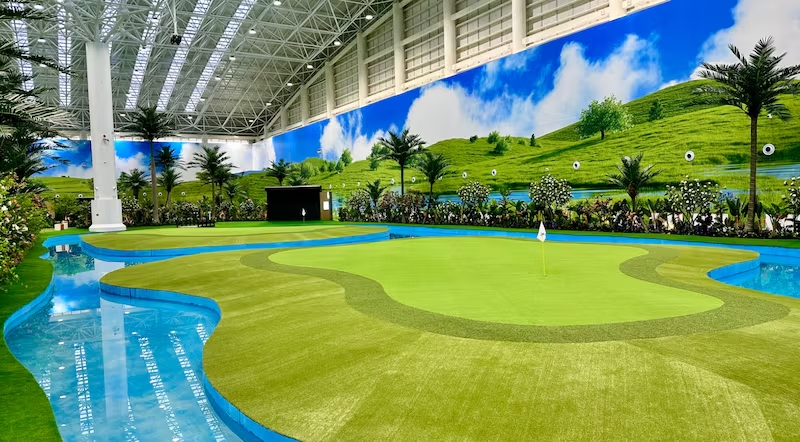 CityGolfの屋内グリーンコンプレックス。人工芝のグリーンと池、壁面に描かれた青空とコース風景