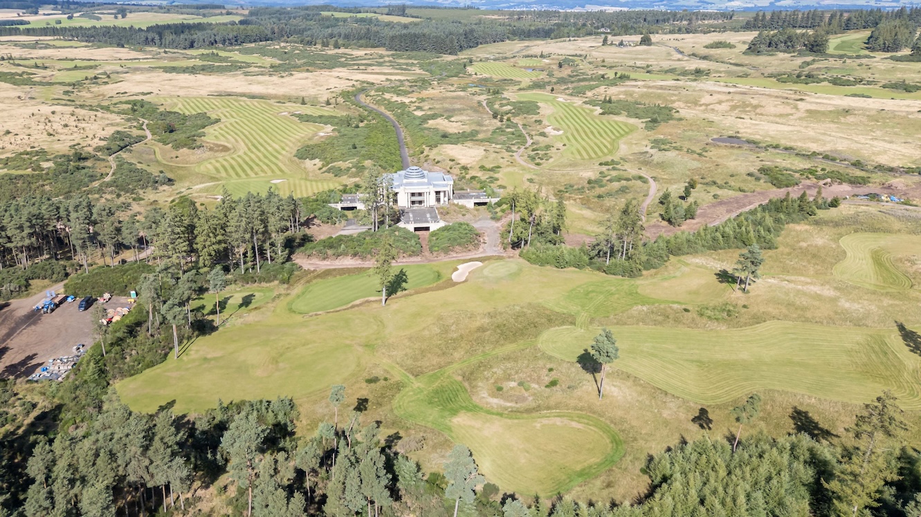 林と草地に囲まれたgWestを上空から撮影した写真。中央にドーム屋根のクラブハウスが建ち、手前と奥に刈り込まれたフェアウェイとグリーンが広がる