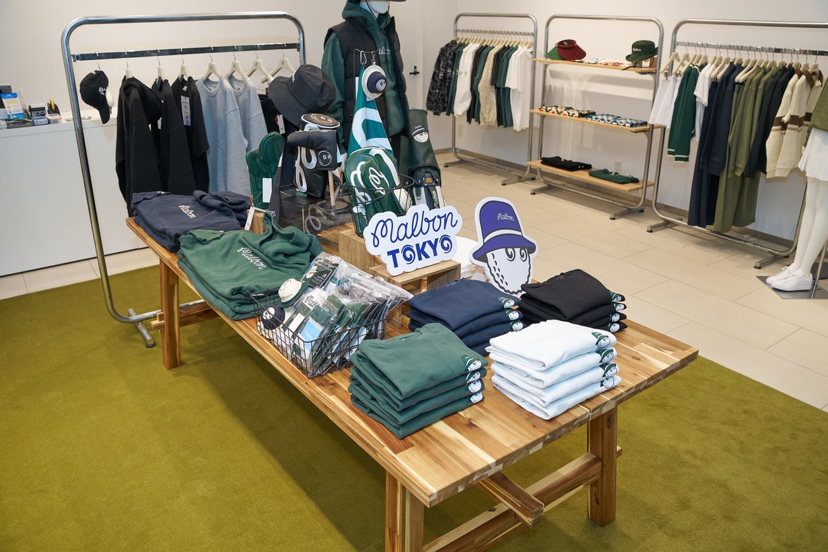 MIYASHITA PARKのMalbon Golfのポップアップ。木のテーブルにウェアが積まれ、ラックに服が並ぶ