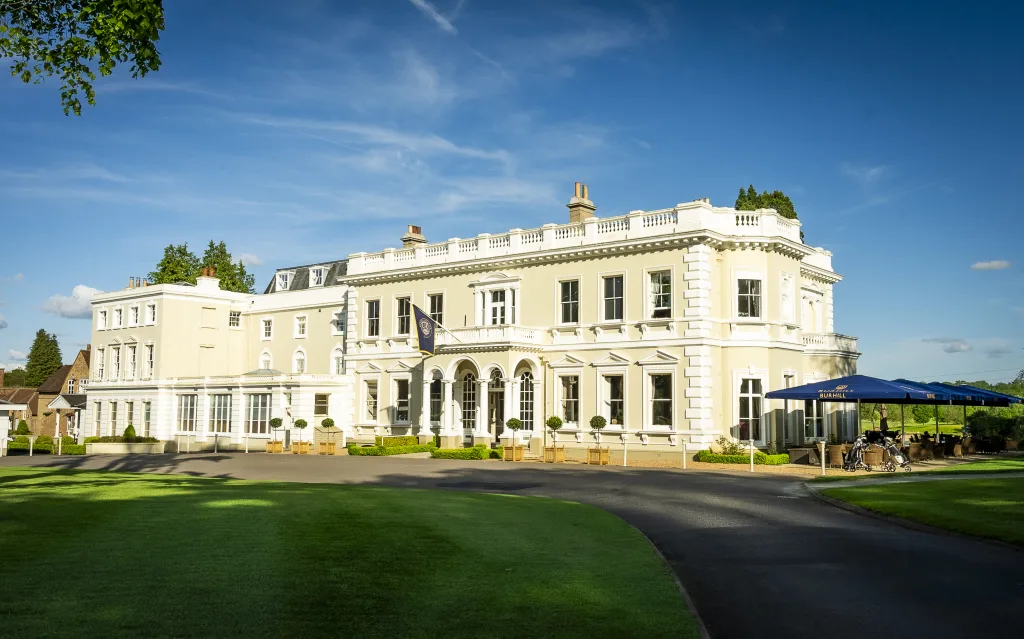 英国サリー州のバーヒル・ゴルフクラブのクラブハウス。白い3階建ての邸宅風の建物と、手前の芝生と車寄せ