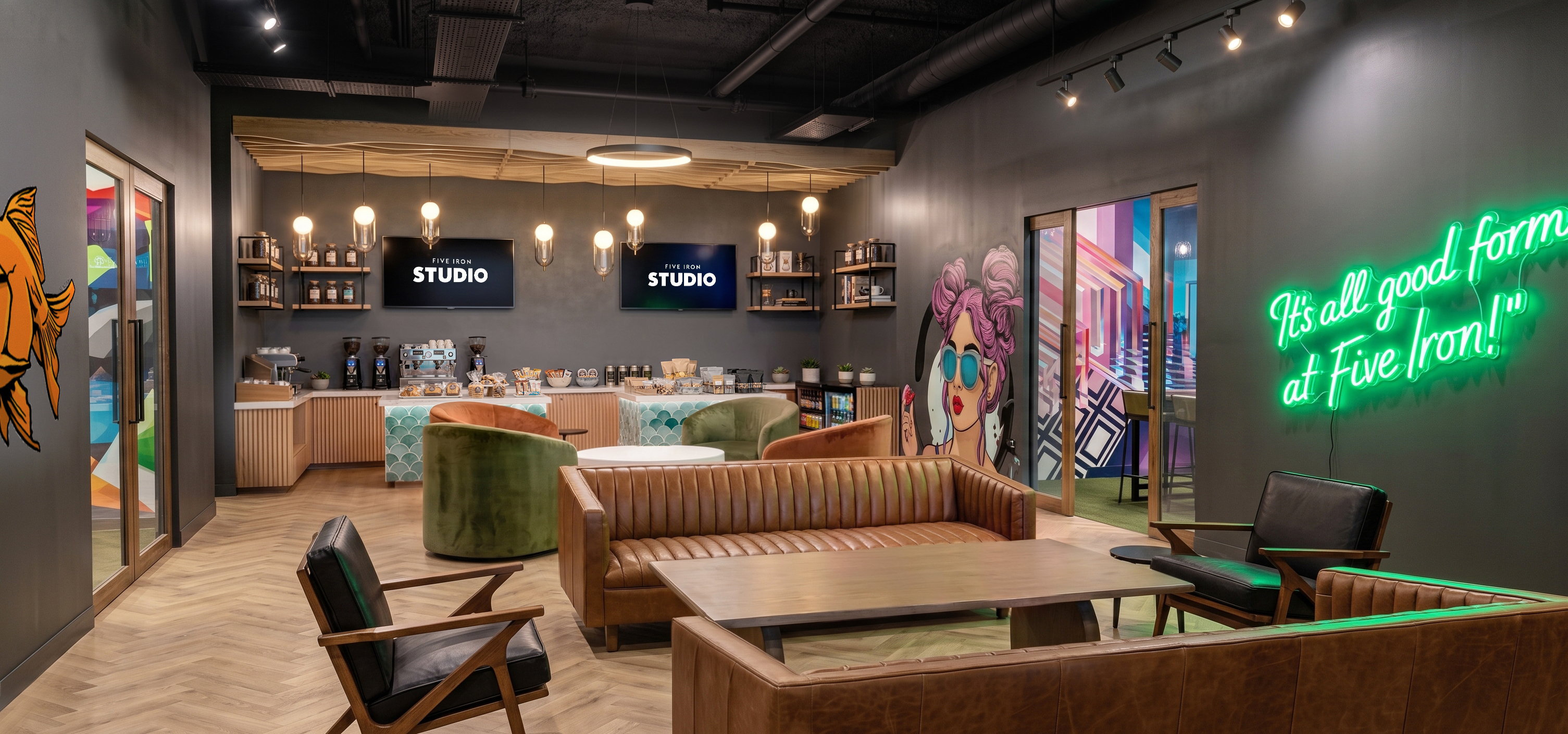 Five Iron Studioのラウンジのイメージ。革張りのソファと椅子、奥に軽食と飲み物の棚、壁にネオンサインと壁画がある