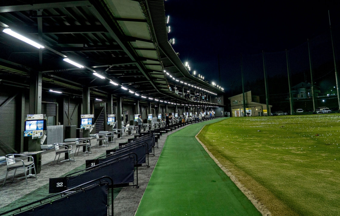 Driving Range BLUEGRASS Oyamada(ブルーグラス大山田、旧リンクス大山田) トップトレーサーのモニター付き打席の列と天然芝フィールド(夜)